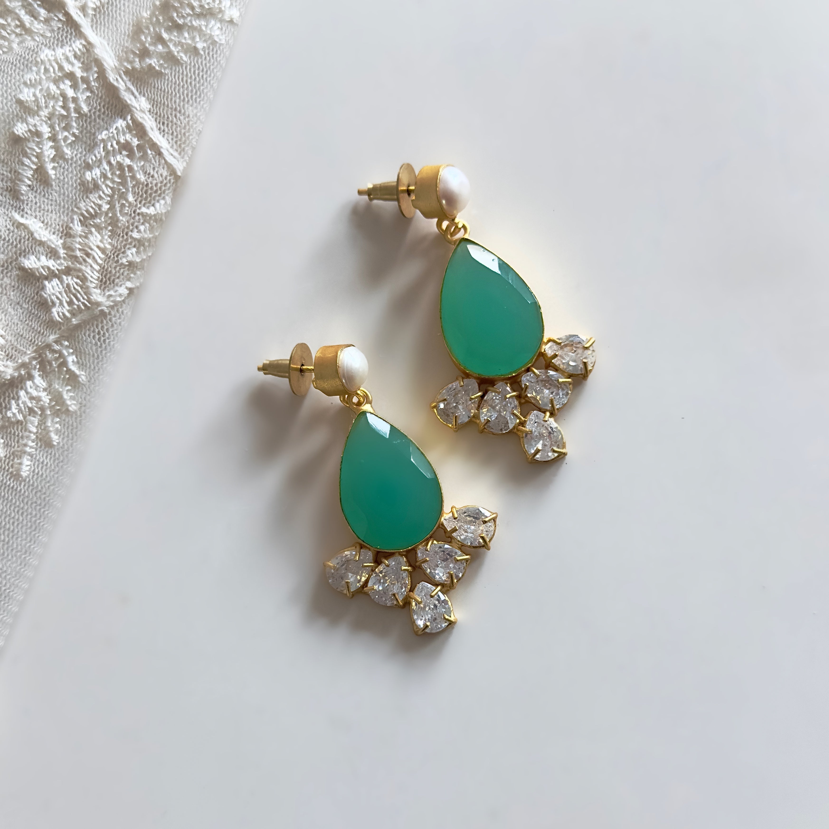 Elevate your style with our Hibah Mint Pearl Drop Earrings. Adorned with a vibrant aquamarine stone and sparkling CZ crystals, these exquisite earrings feature a delicate pearl accent for a touch of sophistication. Add a luxurious touch to any ensemble with these elegant and exclusive earrings.